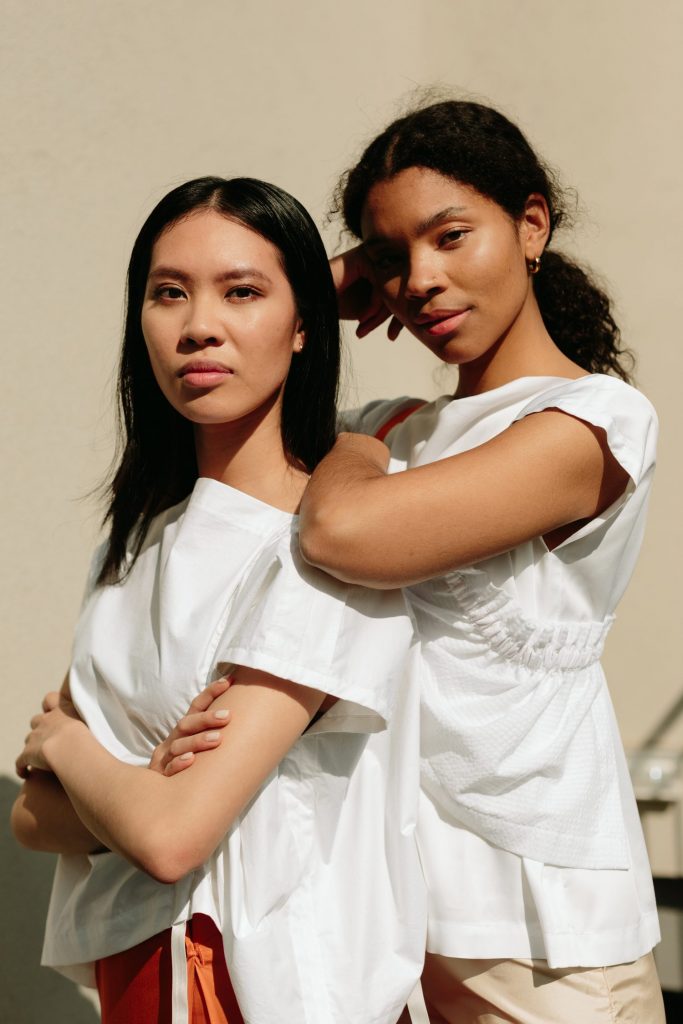 portrettbilde av to kvinnelige modeller, der en lener seg på den andre. Begge er iført hvite bluser.