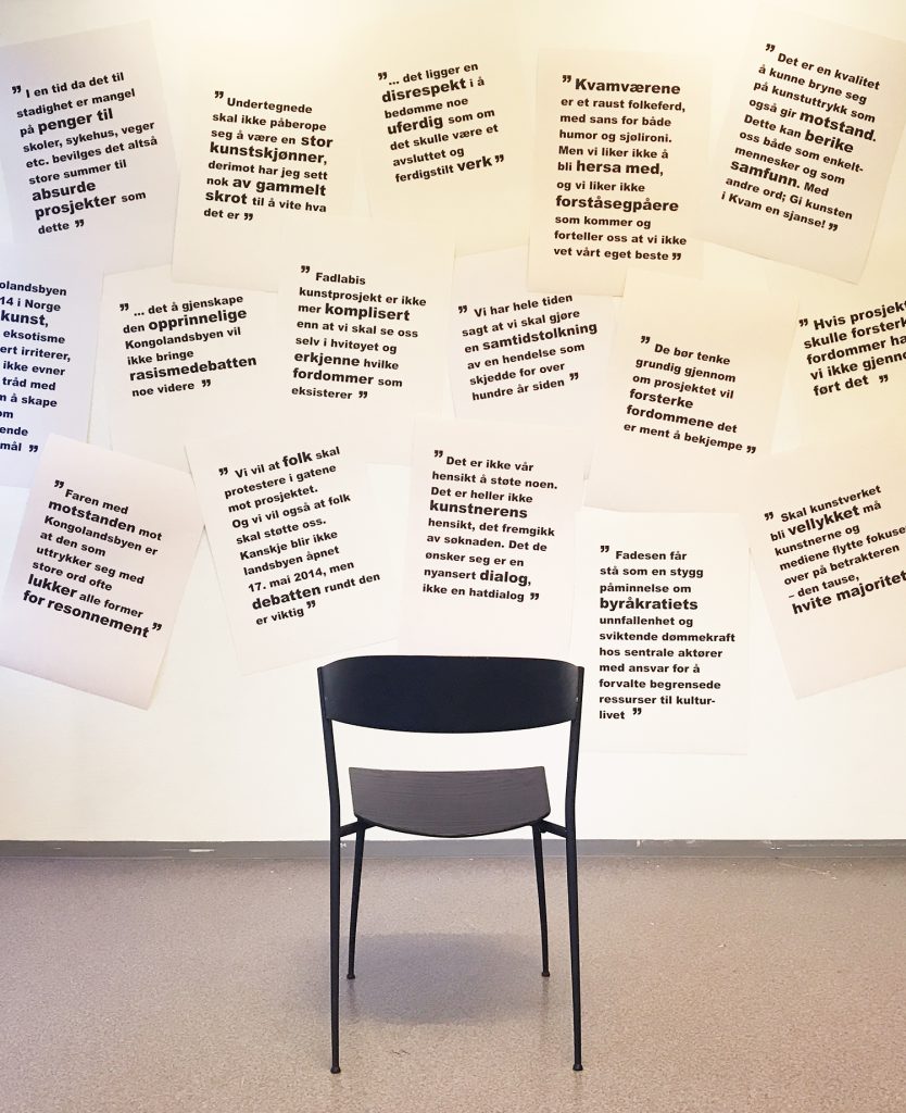 Bilde av installasjon som viser overlappende plakater med sitater på vegg, med en tom stol foran.