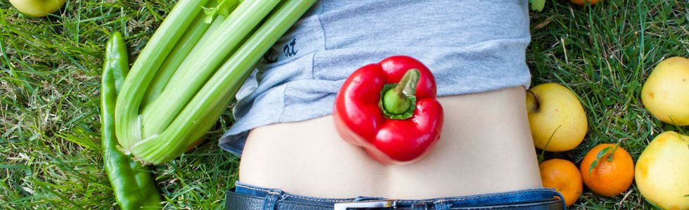 Magen til en liggende person med grønnsaker og frukt strødd rundt. Foto.