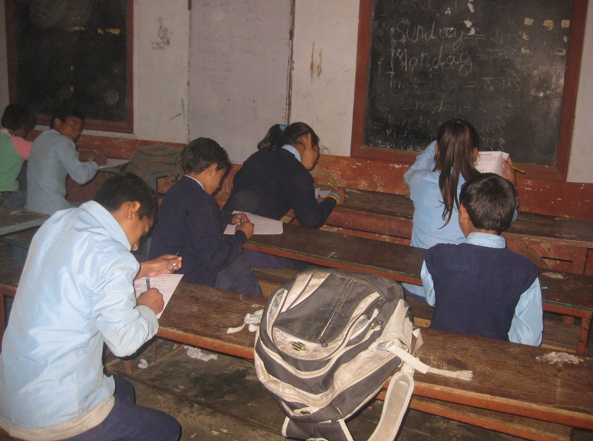 Children in school uniforms in Nepal are filling out a paper-based survey in a classroom.