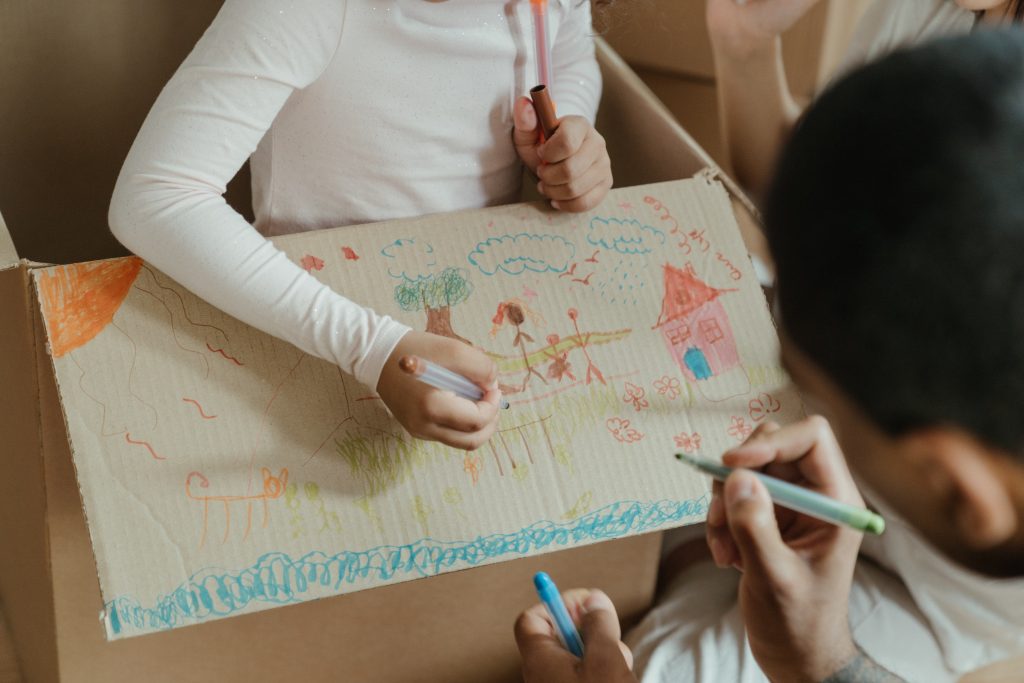 Picture of two kids' hands painting on a paper box.