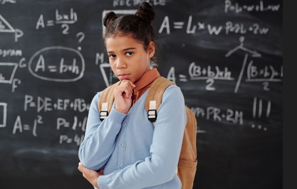 Girl standing thinking in front of a black board.