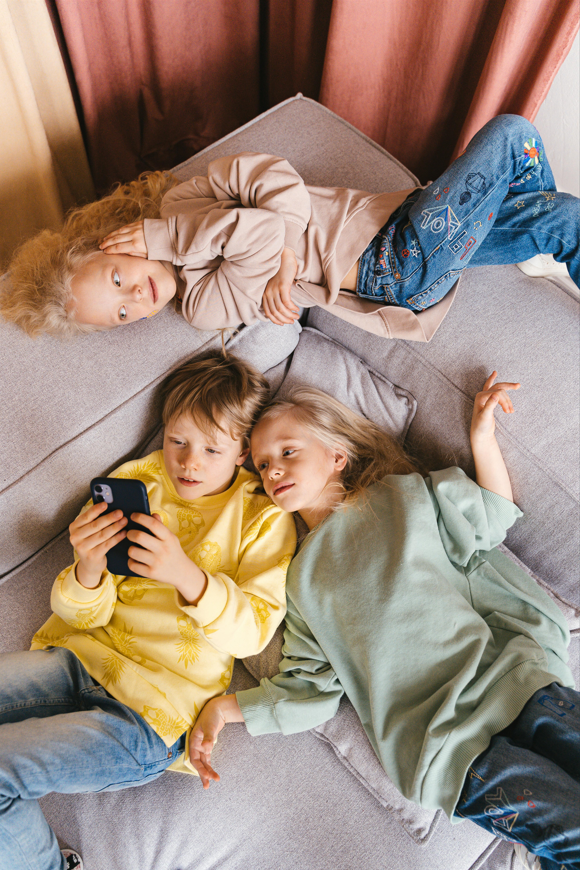 Picture of three children hanging out on a couch looking at a phone