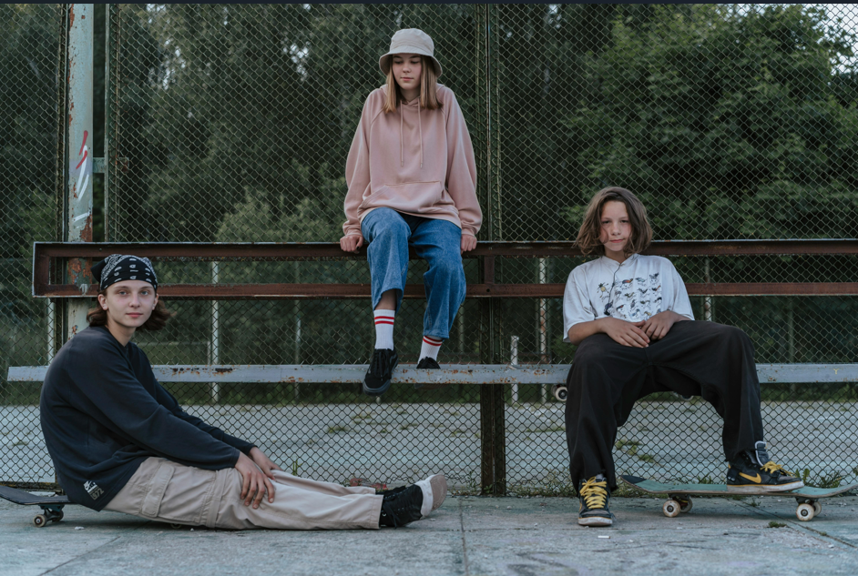 Three tweens sitting outside with skateboards.