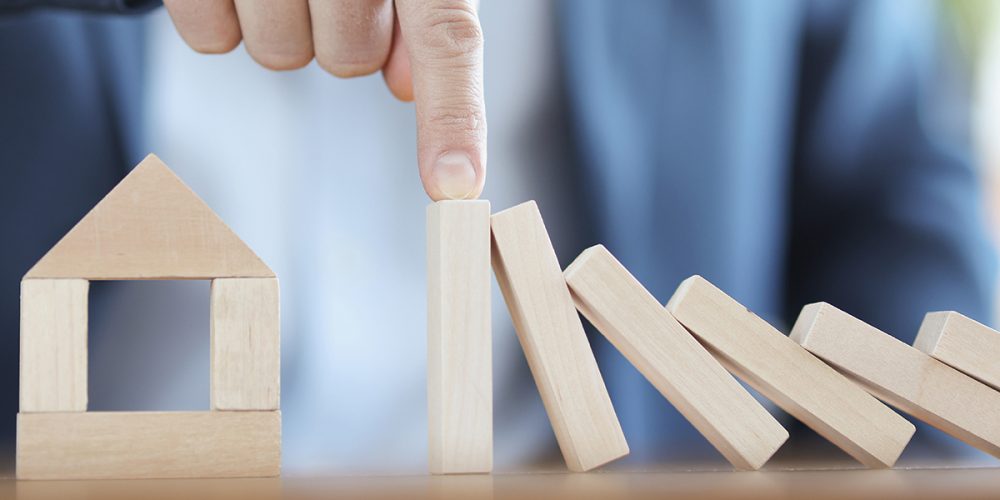 Businessmann holder igjen trebrikker som faller på et hus.