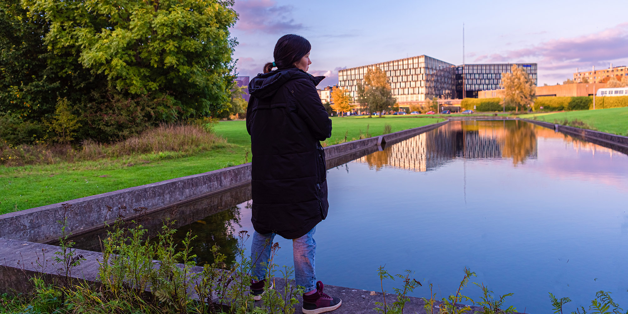 Dame i varme klær står i en park og ser på moderne leilighetsbygg i Danmark