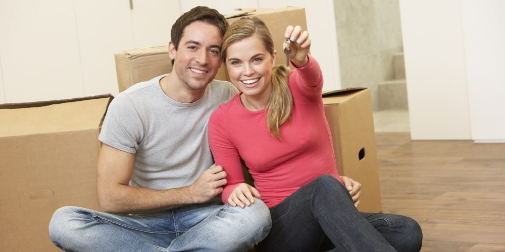 Young couple sit on the floor around boxes holding key in hand