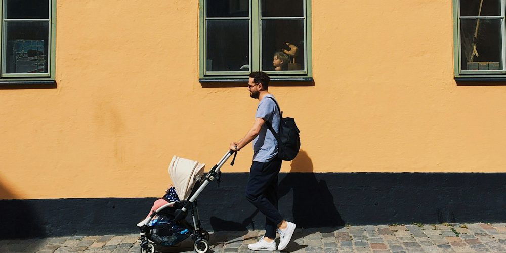 en mann som triller en barnevogn utenfor en blokk