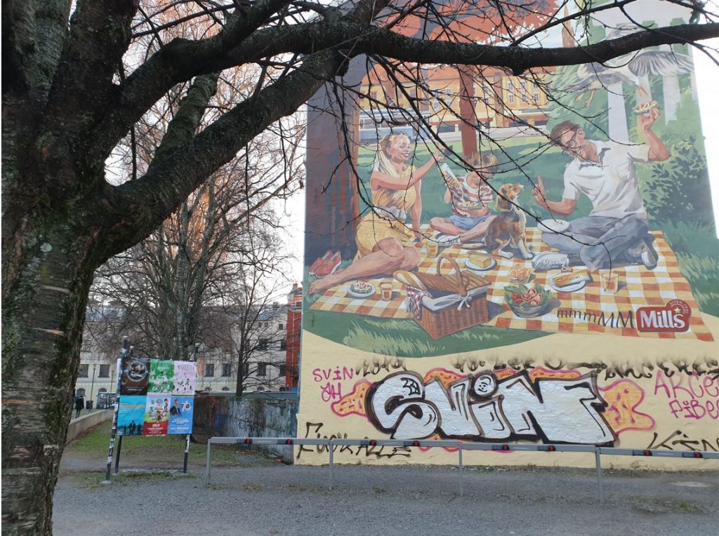 Picture of a mural that is an advertisement of the brand Mills in a street in Oslo with a family eating hotdogs during a picnic. Credit: Ida Tolgensbakk