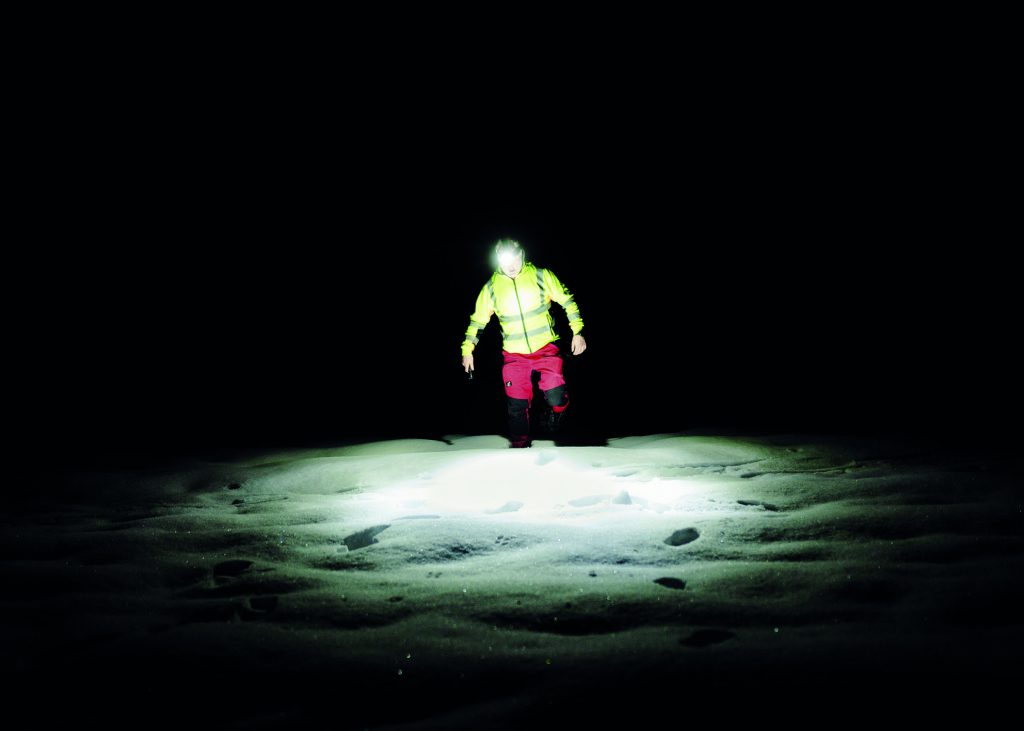lone man walking in the snow at night wearing a headlight