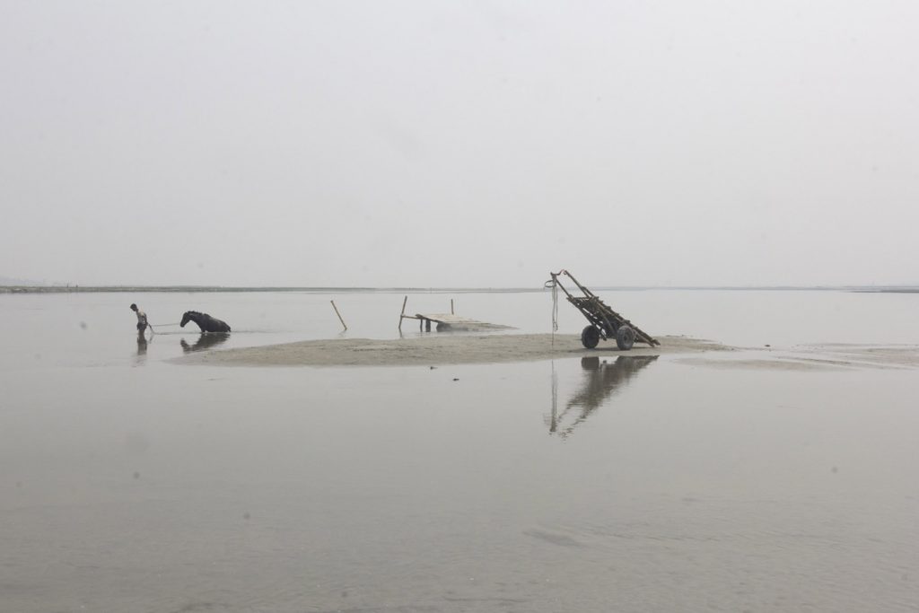 mann walking a hors in the background. in the foreground there is water and a little island.