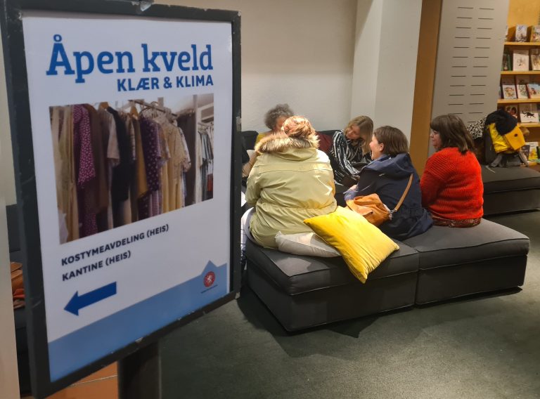 Diskusjon om klær med flere som sitter rundt et bord ed skilt om selve eventet i forkant.
