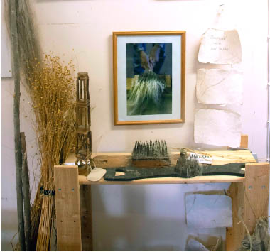 Visar till en del av museet; en träbänk på denne står en äldre häcklar kam i järn, ett rockhuvud i trä även denna ett äldre artefakt. På väggen hänger ett fotografi av ett par händer som häcklar lin. Vid sidan av bänken finner vi torkad lin
