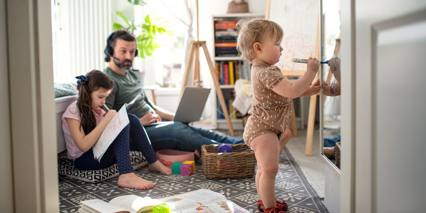 Busy father working with small daughters in bedroom, home office concept.