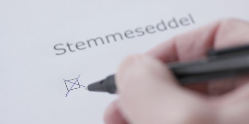 Fingre holder penn som krysser av i boks med bokstaver stemmeseddel over.