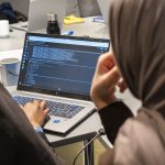 Two girls looking at code on a computer.