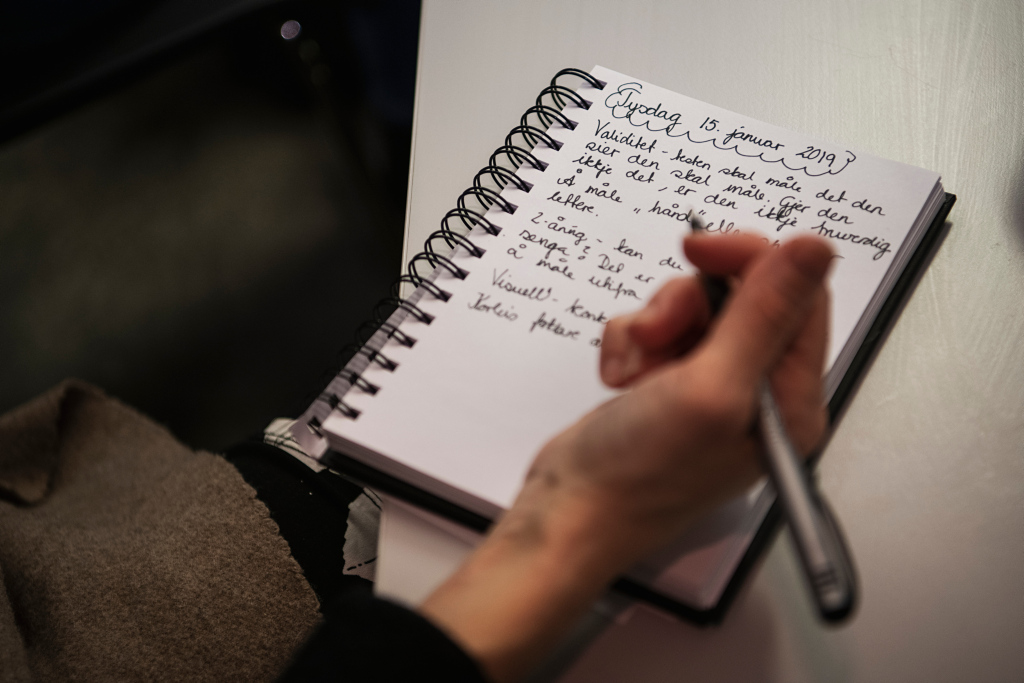 En person skriver for hånd i en notatbok med spiralinnbinding. Teksten handler om validitet og måling