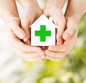 Lite hus med grønt kors. Holdt i hendene til en voksen og et barn. Foto: colourbox.com