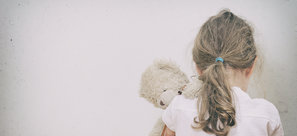 Jente med teddybjørn og ryggen til mot hvit vegg. Foto: colourbox.com