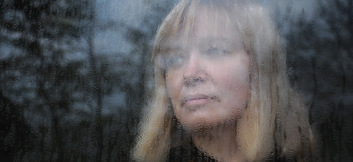 Portrait of the middle-aged woman looking through the window on a rainy day