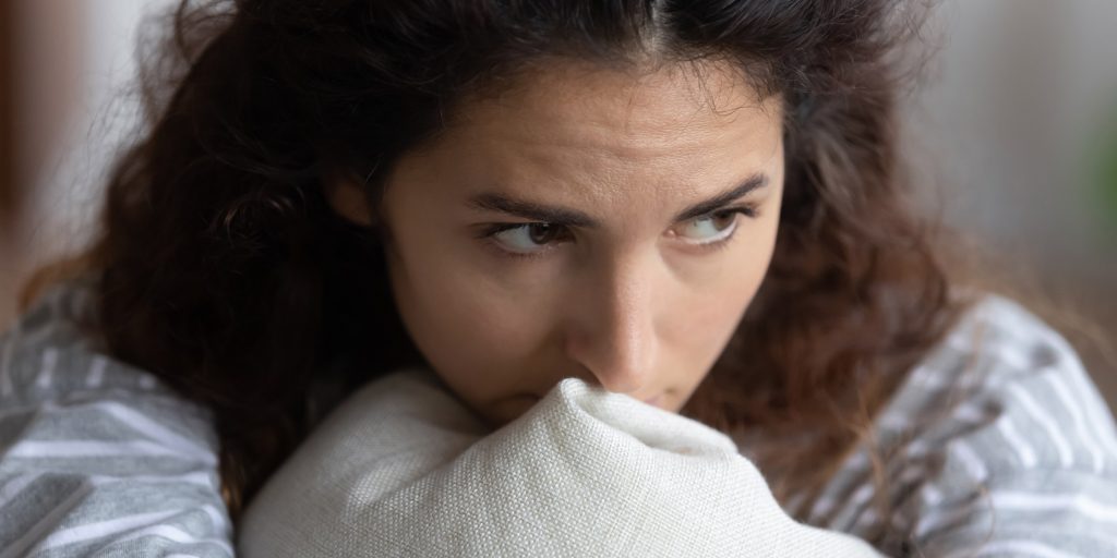 En ung kvinne holder en pute inntil brystet og ser bekymret ut