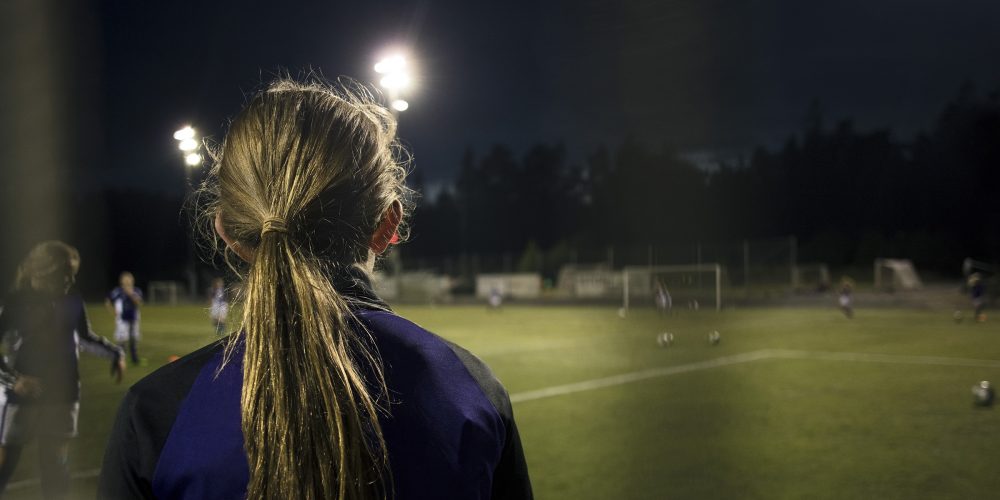 Jente med ryggen til på fotballbane om kvelden