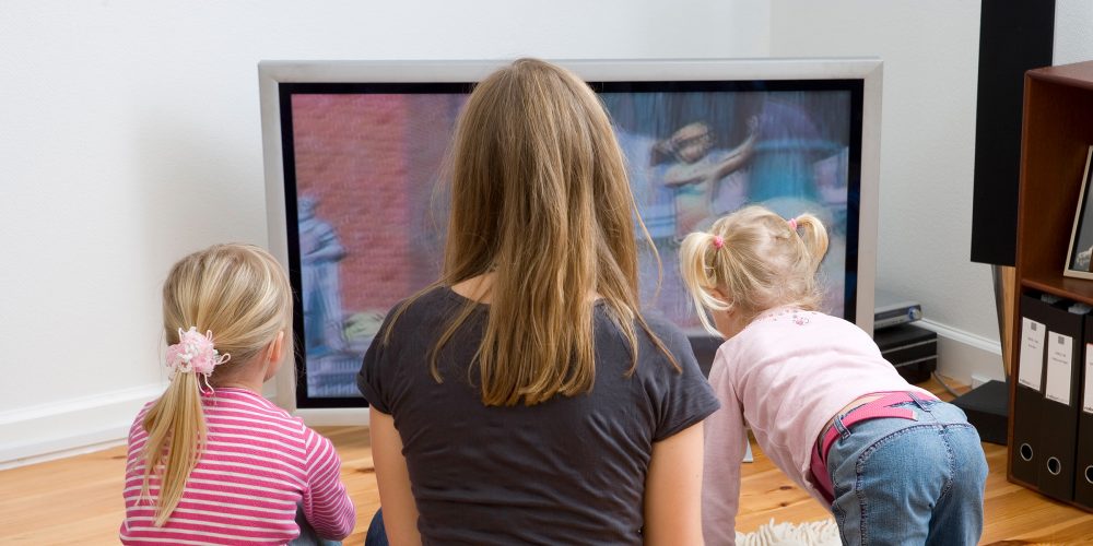 Dame og to barn som ser på tv, ryggen til