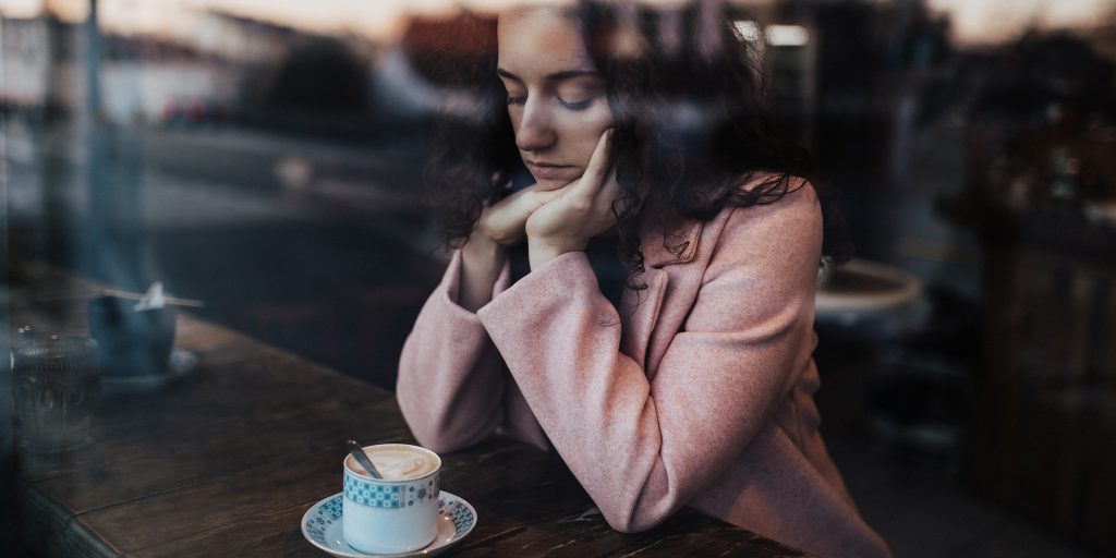 Ung kvinne på kafe ser ned i kaffekoppen